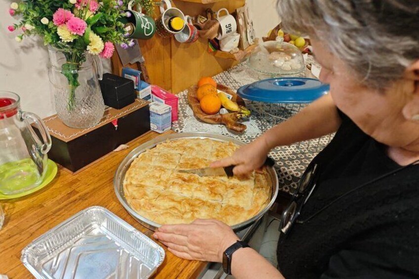En person som serverar en paj på ett träbord, omgiven av olika köksredskap och dekorationer. 1