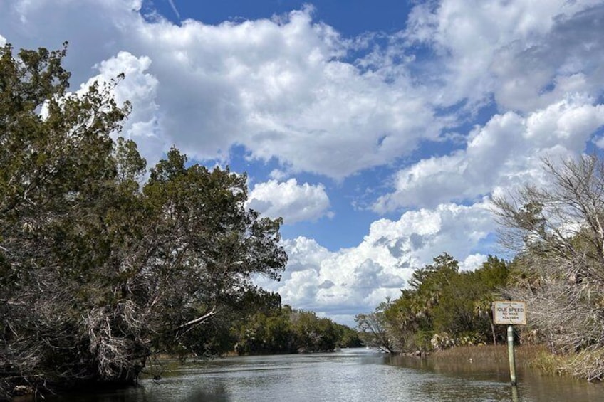 A river with trees on both sides, a partly cloudy sky, and a sign on the right. 1