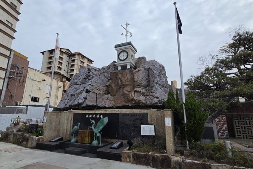 A stone monument with a clock, surrounded by steps and greenery. 5