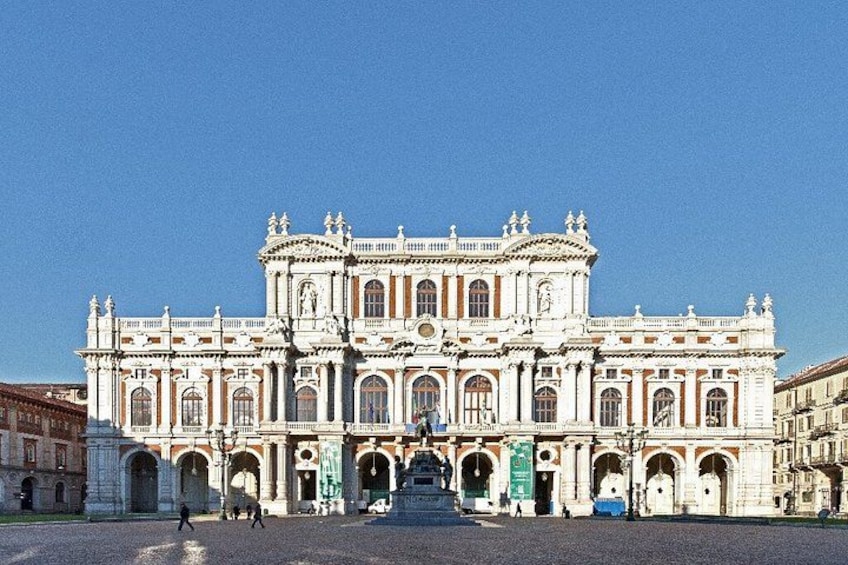 Un edificio grande e decorato, con numerosi archi e colonne, una statua centrale e un cielo azzurro intenso. 4