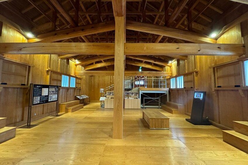 Un vaste espace intérieur en bois, doté d’un haut plafond, de poutres apparentes et d’une colonne centrale. On y trouve des panneaux d’information et un escalier menant à un niveau supérieur. 4