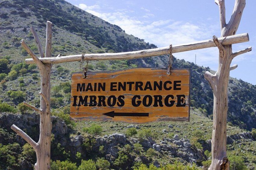 A wooden sign with 'MAIN ENTRANCE IMBROS GORGE' written on it, pointing to the left. 1
