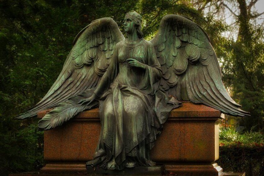 A statue of an angel with wings seated on a stone pedestal in a garden. 5