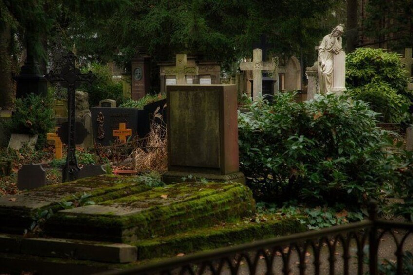 A cemetery with tombstones, a statue, and lush greenery. 3