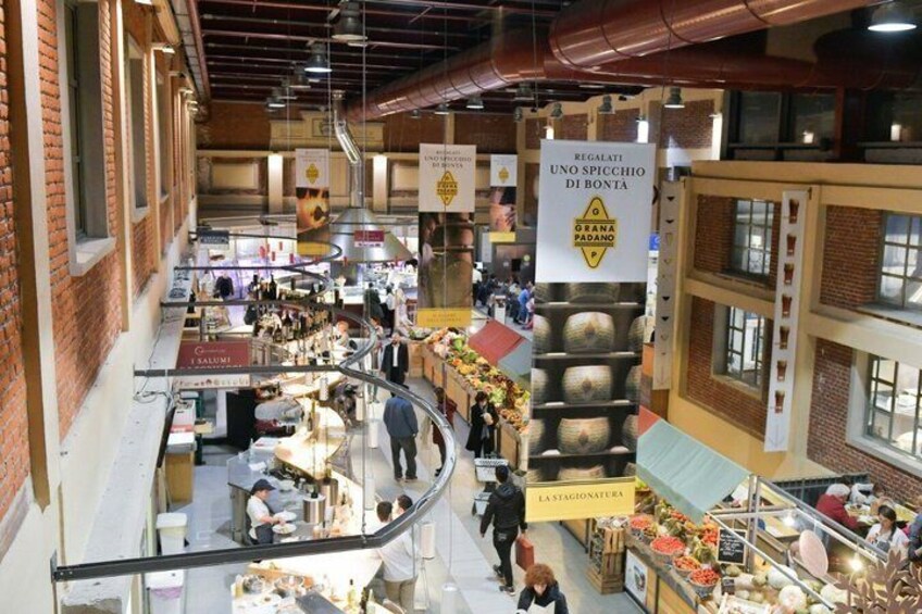 Un mercato al chiuso con diversi banchi, una scala centrale e striscioni appesi. 2