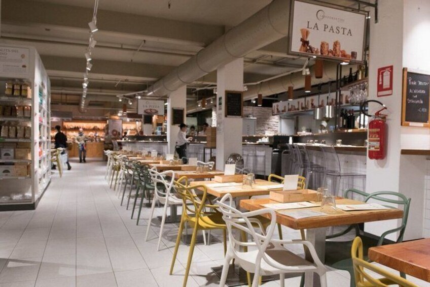 Un interno di un caffè con tavoli, sedie e un'area cucina sullo sfondo. 3