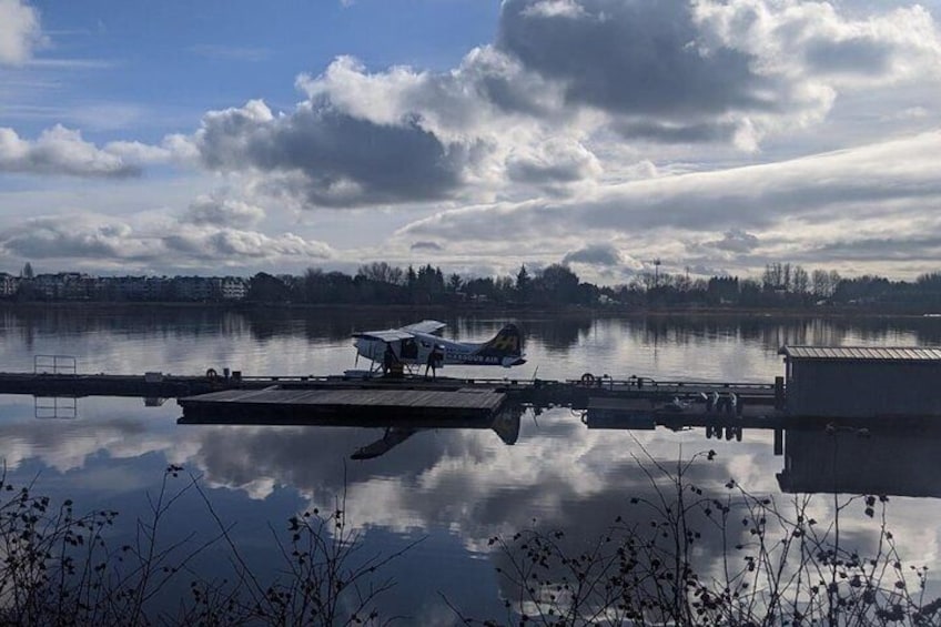 Un lago tranquilo con un muelle, un pequeño avión y un edificio al fondo. 3