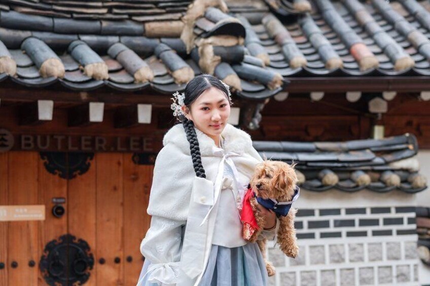 Une personne vêtue d’un costume traditionnel tenant un petit chien devant un bâtiment en bois surmonté d’un toit en tuiles. 3