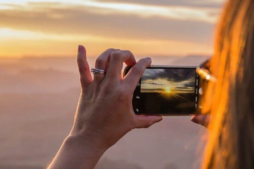 En person håller i en smartphone och fotograferar en solnedgång med moln i bakgrunden. 3