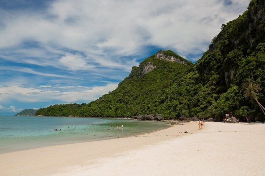 Una playa con agua turquesa cristalina, una orilla arenosa y una montaña verde exuberante al fondo. 5