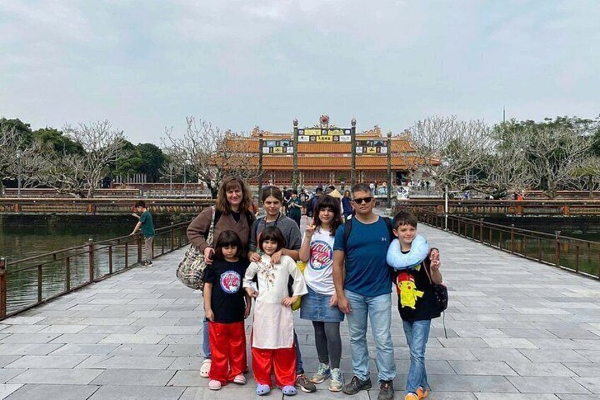 Un groupe de personnes se trouve sur un pont, avec une étendue d’eau et un bâtiment traditionnel en arrière-plan. 5