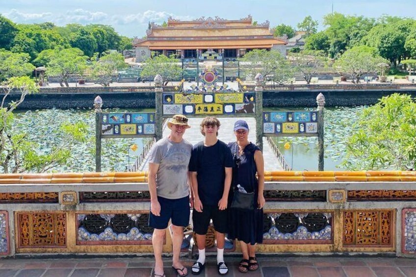 A group of people standing on a bridge with a decorative railing and a temple in the background. 3