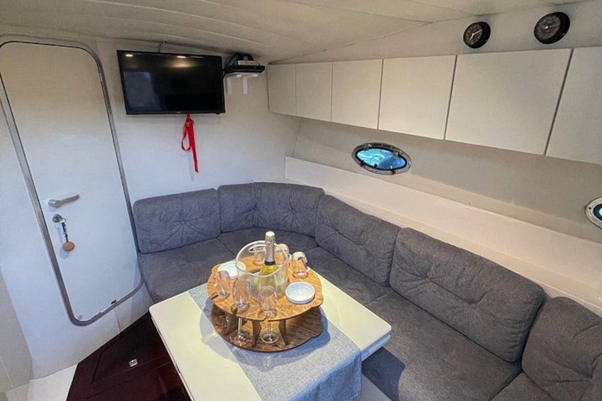 Un espace de vie compact comprenant un canapé gris, une petite table agrémentée d’un élément décoratif, un téléviseur fixé au mur et une porte dotée d’une poignée. 3