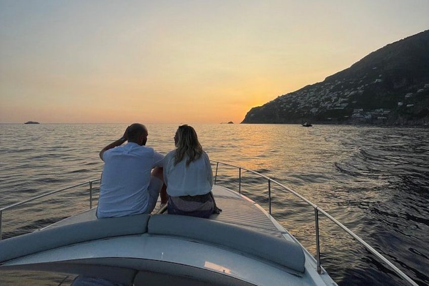 Deux personnes assises sur un bateau, face à la mer, au moment du coucher du soleil. 5