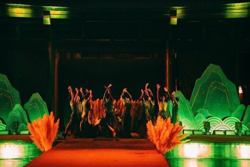 A stage with dancers performing in a dimly lit setting with green and orange lighting. 4