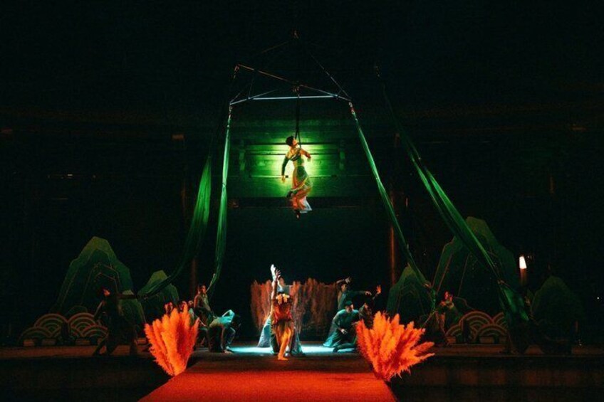A stage with a performer suspended in the air, surrounded by green curtains and a red carpet. 2