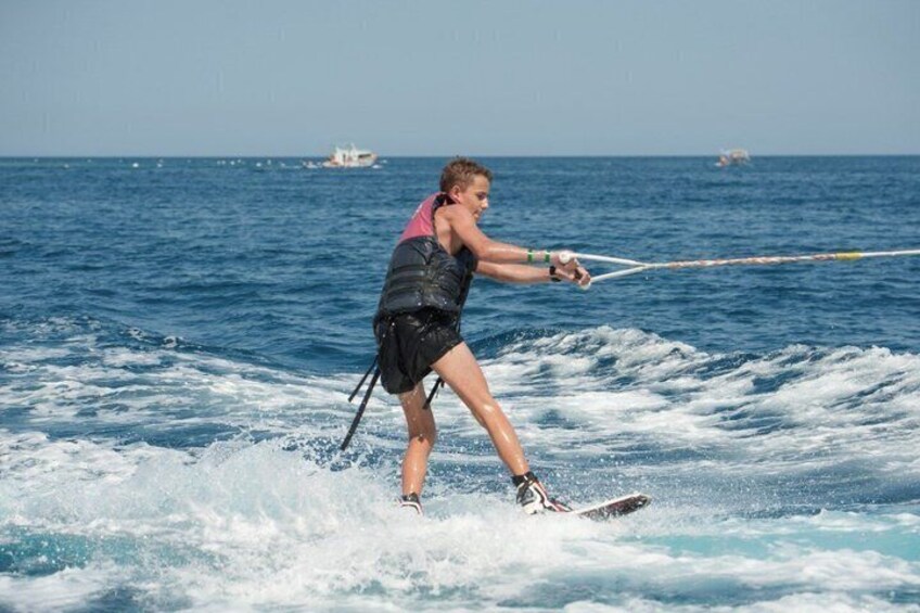 Iemand wakeboard op een wateroppervlak met golven, draagt een reddingsvest en houdt een touw vast. 2