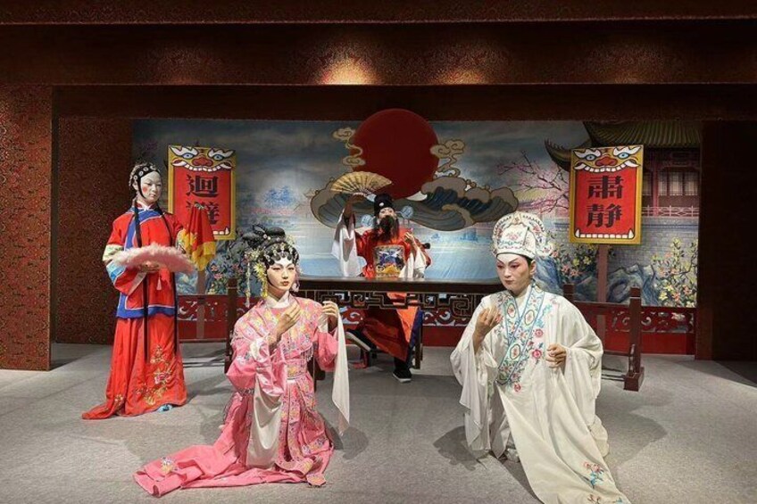 Un escenario con cuatro personas vestidas con trajes tradicionales, un telón de fondo pintado y un abanico rojo. 2