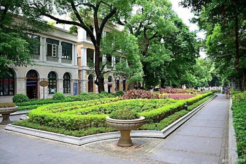 Un jardín cuidado con setos geométricos, un sendero y un edificio con ventanas arqueadas. 4