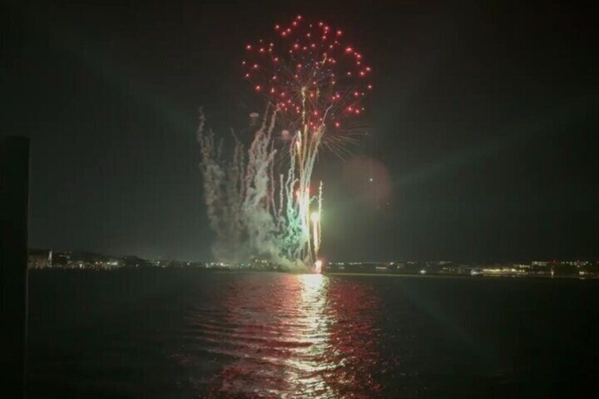 A nighttime fireworks display over a body of water with reflections on the surface. 1