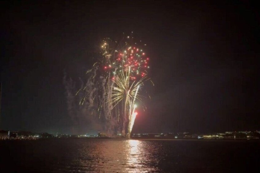 A nighttime fireworks display over a body of water with reflections on the surface. 4