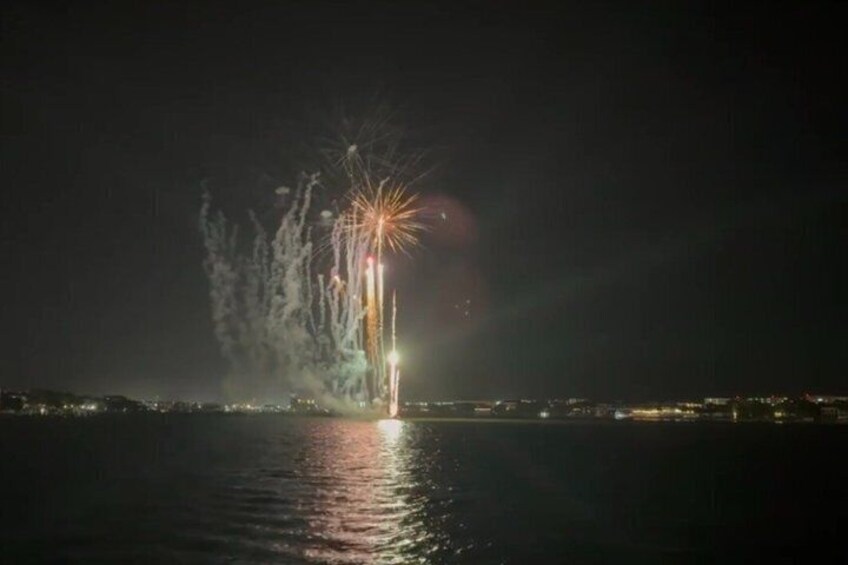 A nighttime fireworks display over a body of water with reflections on the surface. 2