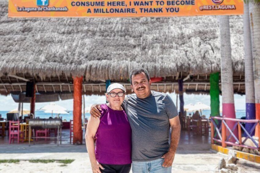 Dos personas de pie frente a un restaurante en la playa con techo de paja. 3