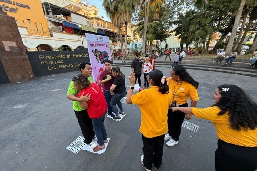 Un groupe de personnes vêtues de chemises jaunes effectue une danse dans un espace public en plein air, avec des palmiers et un bâtiment en arrière-plan. 4