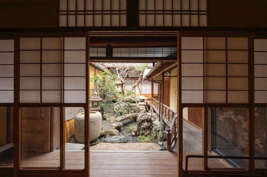A traditional Japanese interior with tatami flooring, sliding doors, and a view of a garden with rocks and a wooden bridge. 5