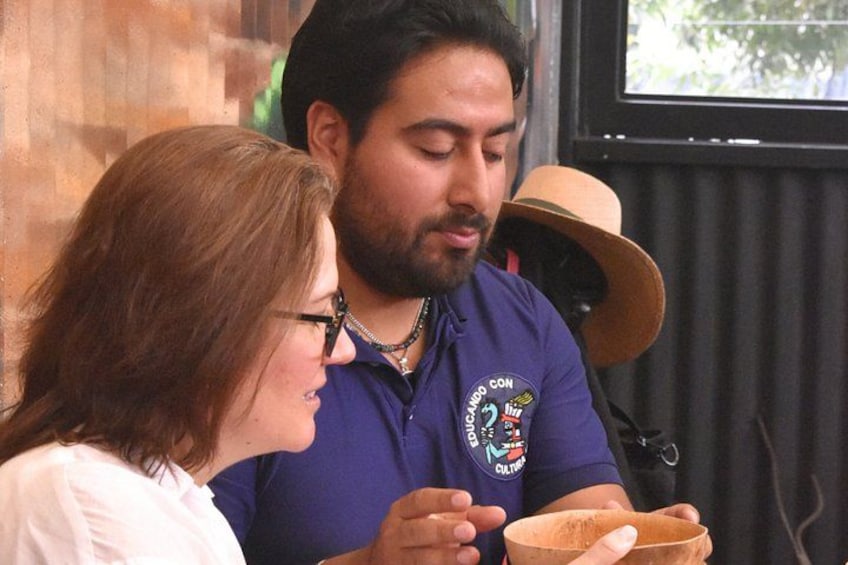 Una persona con una camisa morada con un logotipo, sosteniendo un tazón y una cuchara, en una habitación con una ventana y un sombrero sobre una silla. 5