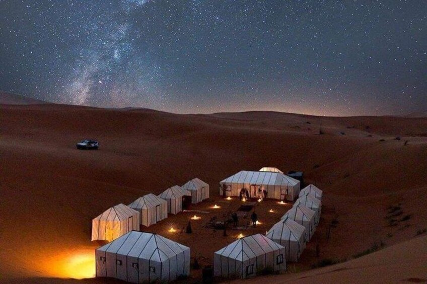 A desert with yurts and a car under a starry sky. 3