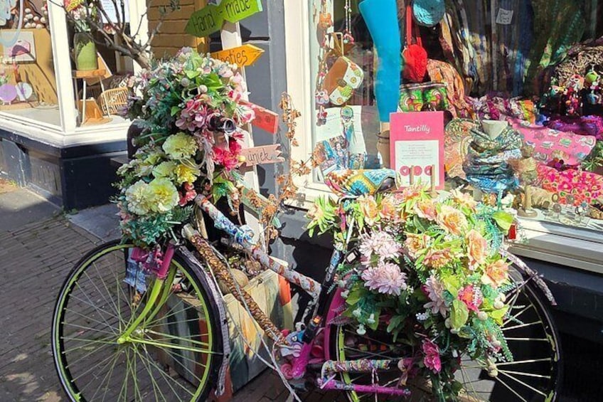 Una bicicleta adornada con flores y cintas, estacionada frente a una tienda. 1