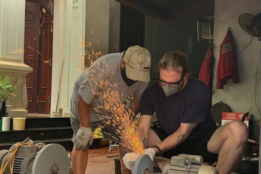 Two men working with a power tool, sparks flying, in a workshop with tools and equipment around. 1