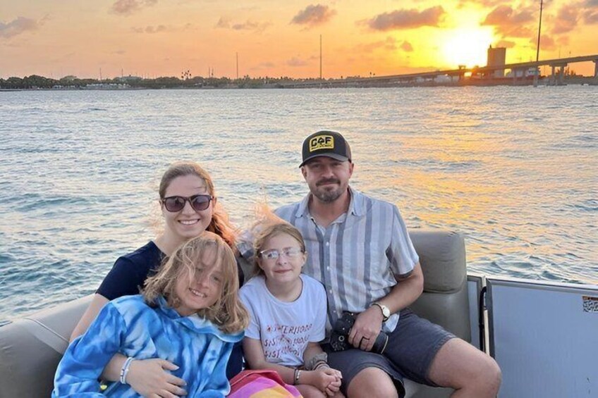 Una familia en un barco, con un atardecer y un puente al fondo. 2