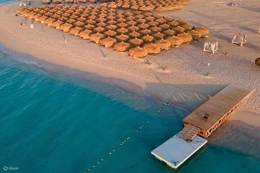 Una spiaggia con ombrelloni di paglia, un molo di legno e acqua cristallina color turchese. 2
