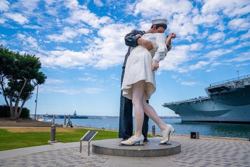 Une statue représentant un marin et une femme, avec un navire en arrière-plan et un ciel dégagé. 1