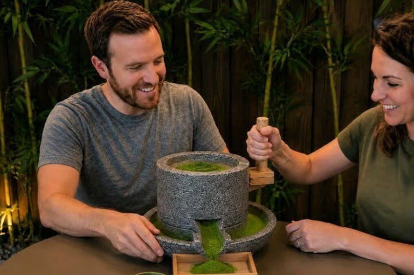 Dos personas en una mesa con un mortero y maja de piedra, rodeadas de plantas de bambú. 1