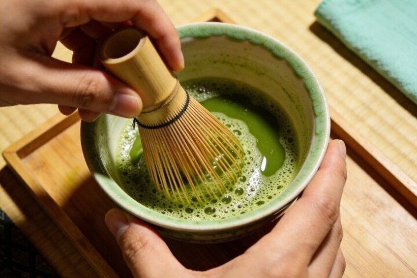 Hænder pisker matcha i en grøn skål. 1
