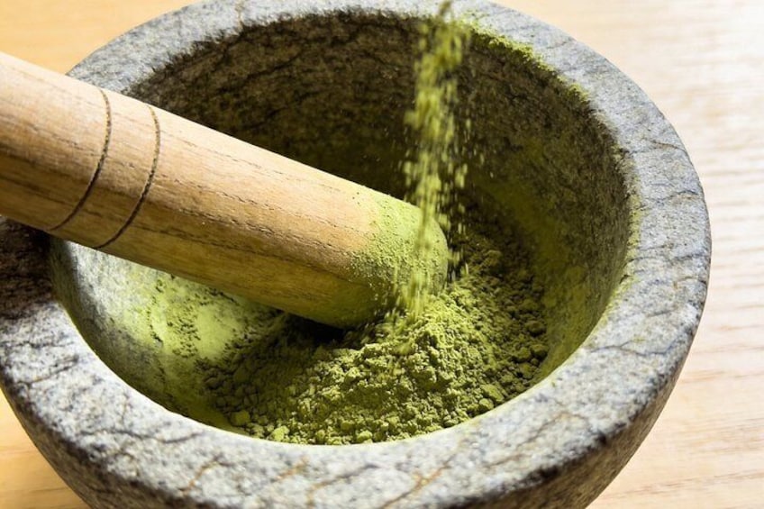 Un mortero de piedra con un mortero de madera y polvo verde, probablemente matcha, siendo molido. 5