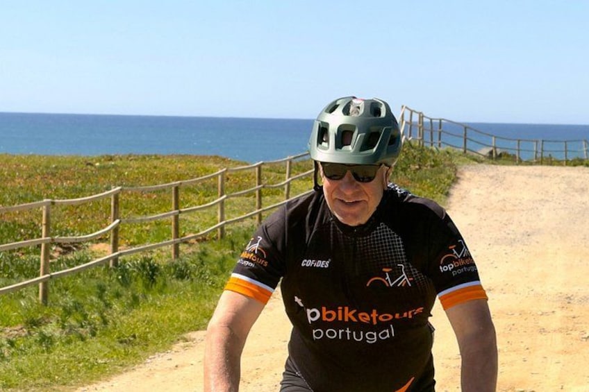 A cyclist on a dirt path with a wooden fence and the ocean in the background. 2