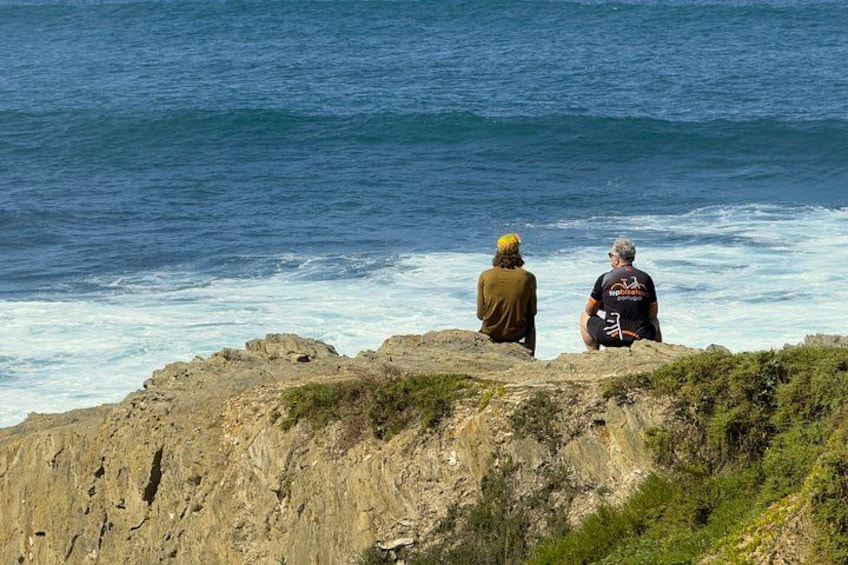 Two people sitting on a rocky cliff overlooking the ocean. 1