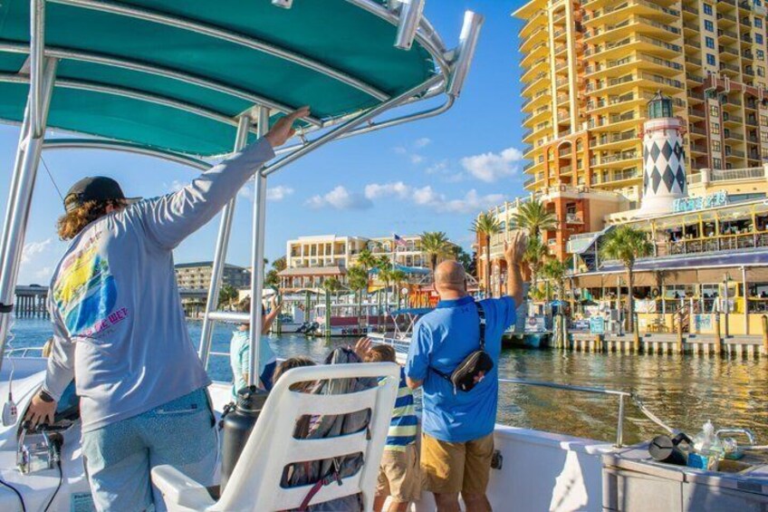 A boat with two people, one pointing towards a tall building with a lighthouse, and another pointing towards the water. 2