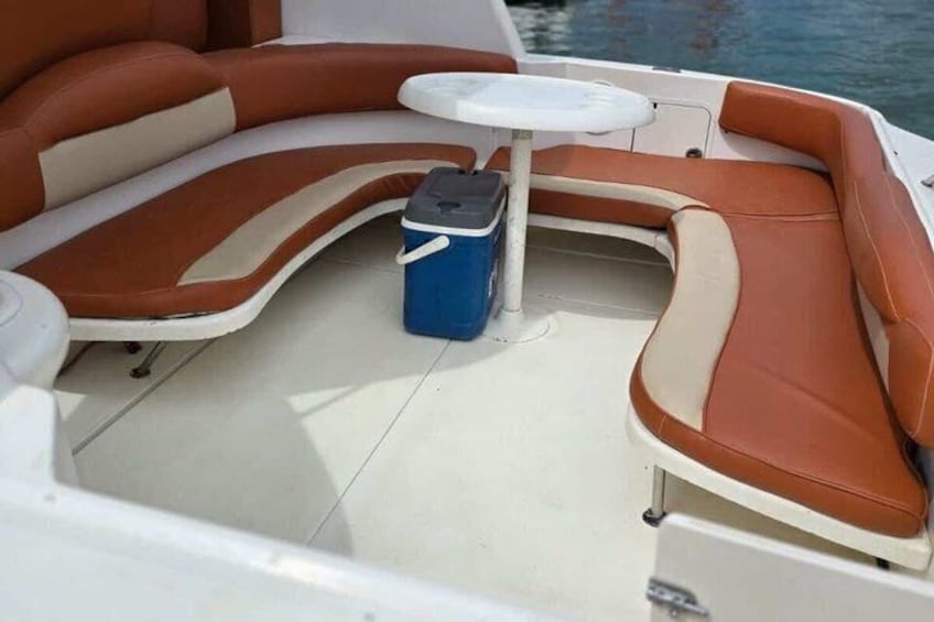 Interior de un barco con una zona de estar curvada, una mesita y un enfriador. 4