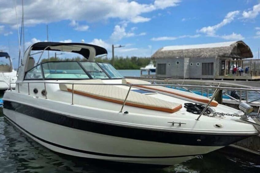 Un barco a motor blanco amarrado en un puerto deportivo, con una estructura de techo de paja al fondo. 1