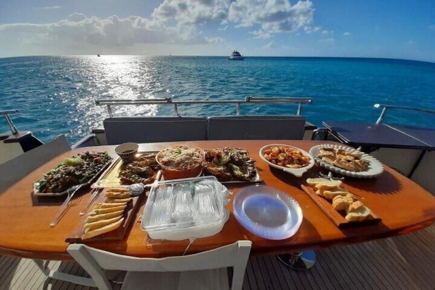 Una mesa con diversos platos en un barco con vista al océano y un barco a lo lejos. 2