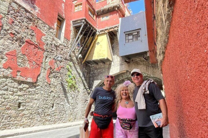 A narrow street with a stone wall, red graffiti, and a building with a yellow awning. 2