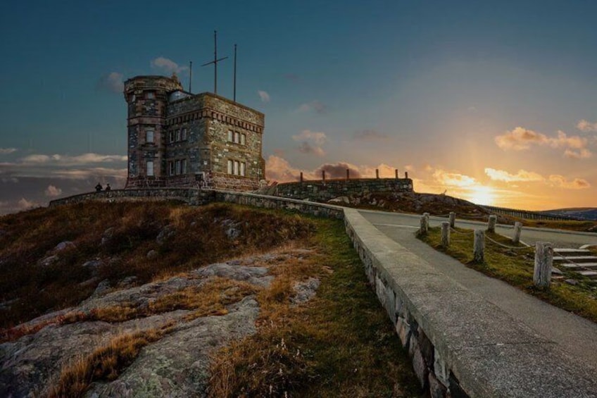 Une tour de pierre ornée de croix, un chemin pavé et un coucher de soleil en arrière-plan. 2