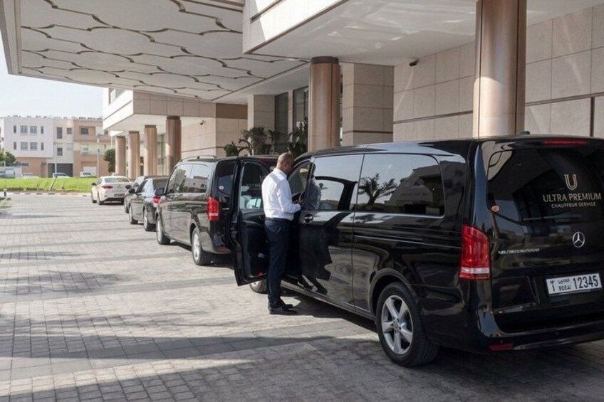 A black van parked in front of a building with columns, a man standing next to it, and other vehicles in the background. 3