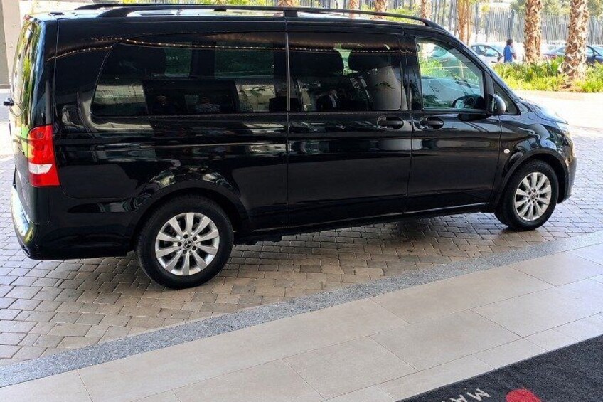 A black van parked on a paved area with a tiled walkway and a curb. 2