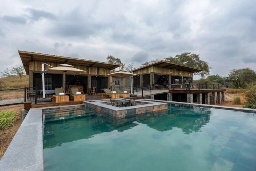 A pool with a wooden deck, lounge chairs, and a covered outdoor area. 2